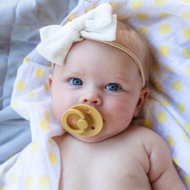 Kūdikis su geltonu Bibs čiulptuku burnoje