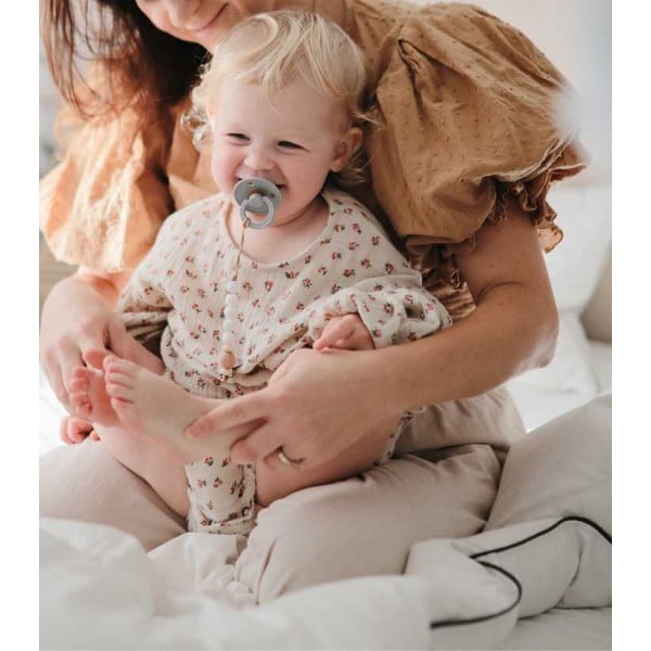 Laimingas kūdikis ant mamos rankų su Bibs čiulptuku