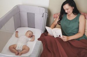 Mama skaitanti knygą prie ramiai miegančio kūdikio