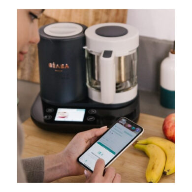 Mama naudoja Béaba ir Me programėlę telefone šalia Babycook Smart prietaiso virtuvėje