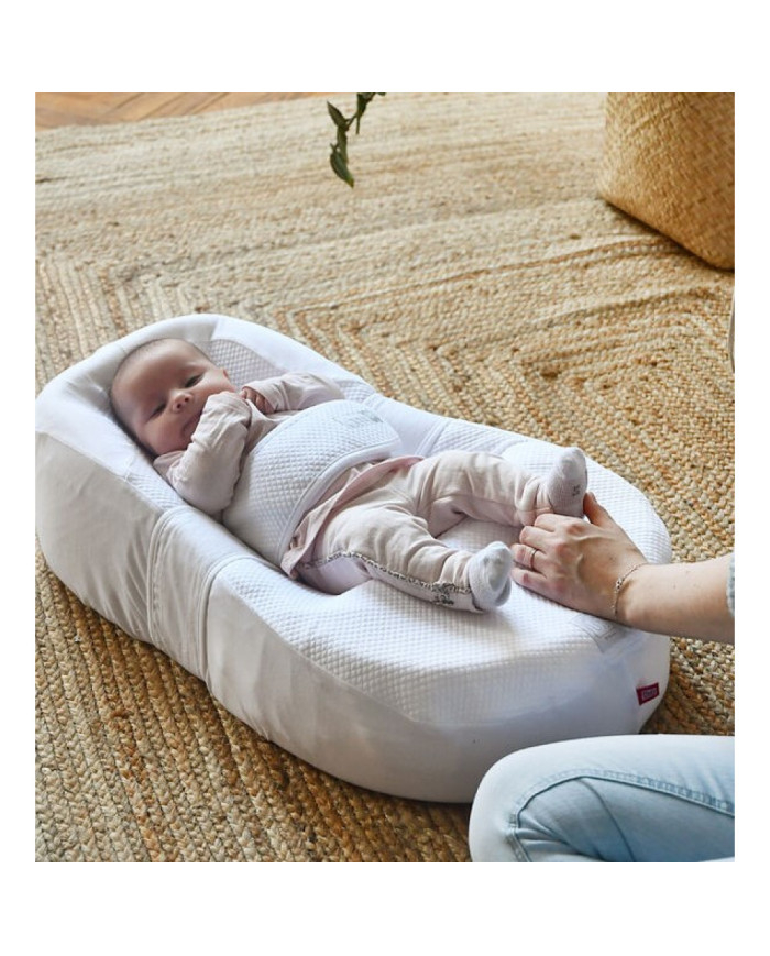 Kūdikis guli baltame Cocoonababy gultuke ant pintos kilimėlio mama laiko kojytes
