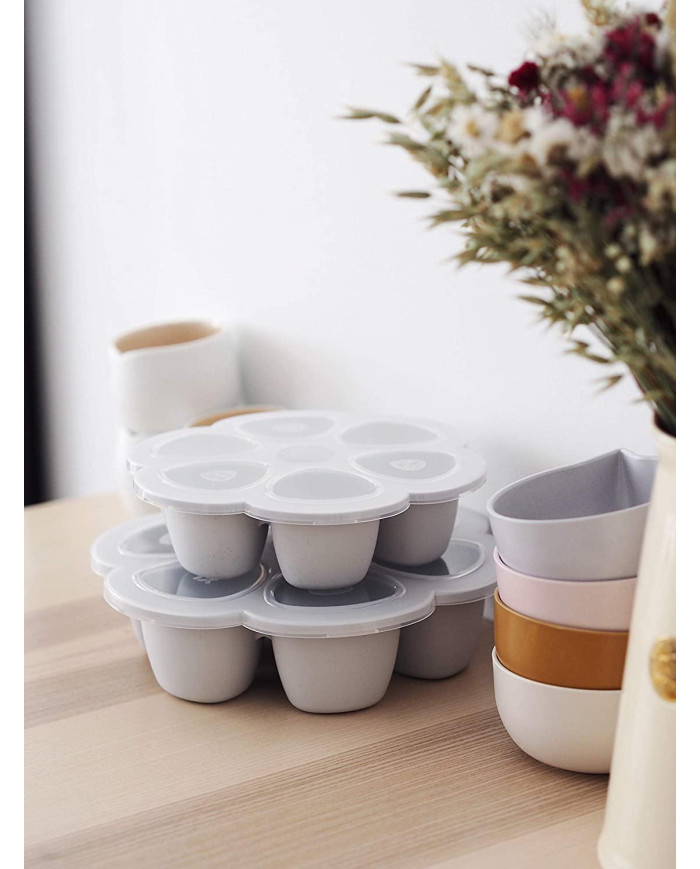 Dvi sustatytos BEABA Multiportions XL silikoninės formos ant medinio stalo šalia dubenėlių ir gėlių puokštės
